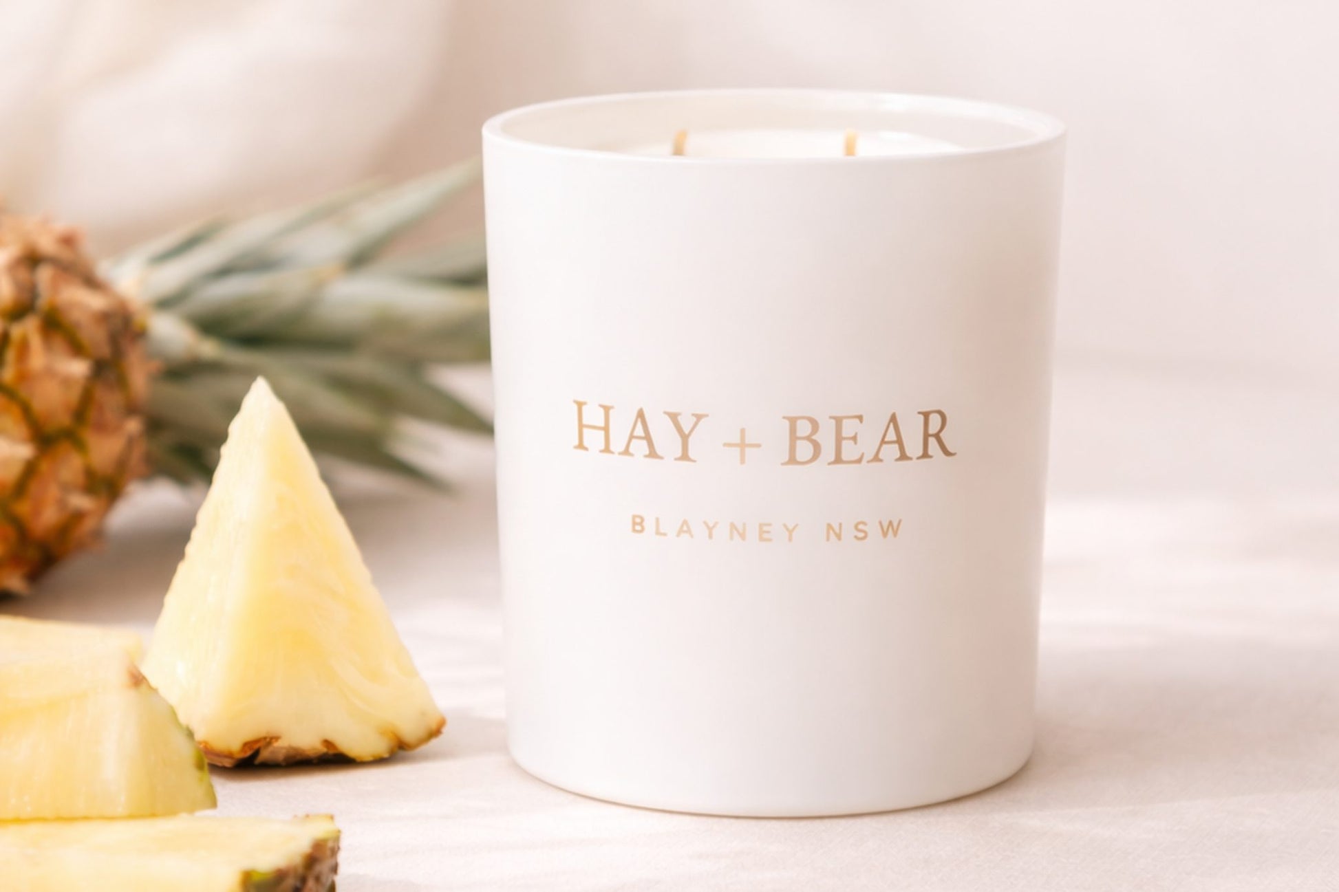 White candle with 'Hay + Bear' branding next to pineapple slices on a light background