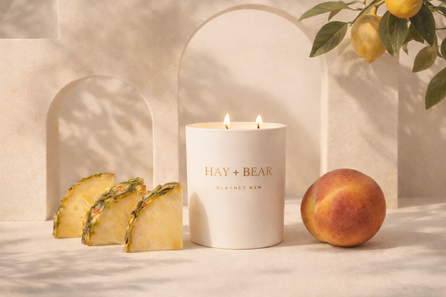 Hay + Bear candle with pineapple slices, lemon, and peach on a neutral background